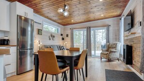 A modern kitchen with a stainless steel refrigerator, wooden ceiling, and a dining area with a table and chairs. - Hôtel à la maison - Le Cocon, ski et golf (Adstock)