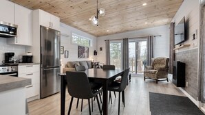 A modern kitchen with a dining area, wooden ceiling, and a fireplace. - Hôtel à la maison - La Cachette, golf et ski! (Adstock)