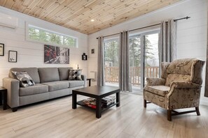 A living room with a sofa, armchair, coffee table, and a large window with curtains. - Hôtel à la maison - La Cachette, golf et ski! (Adstock)