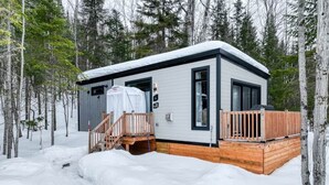 A cabin with a wooden deck, a covered porch, and a snow-covered ground. - Hôtel à la maison - La Cachette, golf et ski! (Adstock)