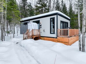 A cabin with a wooden deck, a covered porch, and a snow-covered ground.