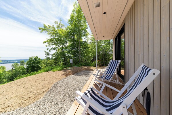 Una terraza de madera con dos sillones reclinables a rayas frente a una vista panorámica de un lago y un bosque.
