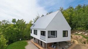 Una casa moderna de dos pisos con techo inclinado, ventanas grandes y una terraza de madera.
