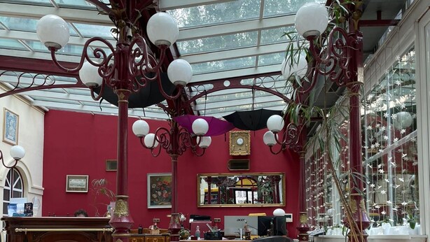 A conservatory with a red interior, featuring a wooden desk, two black sofas, and a coffee table. - Hotel Viki (Vienna)