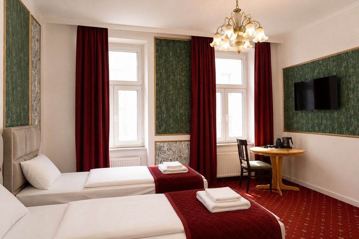 A hotel room with two beds, a desk, a chair, a television, and a window with curtains.