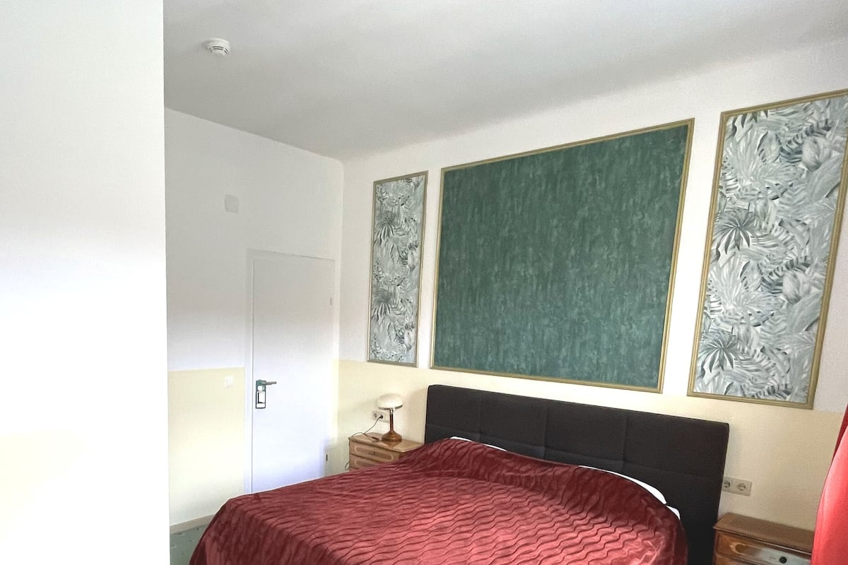 A bedroom with a bed, a nightstand, a desk, and a door.