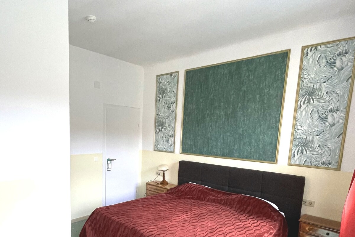 A bedroom with a bed, a nightstand, a desk, and a door.