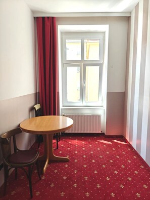 A small room with a round wooden table and two chairs, a radiator, and a window with curtains. - Hotel Viki (Vienna)