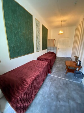 A room with two beds, a wooden table with a kettle, and a trash bin. - Hotel Viki (Vienna)