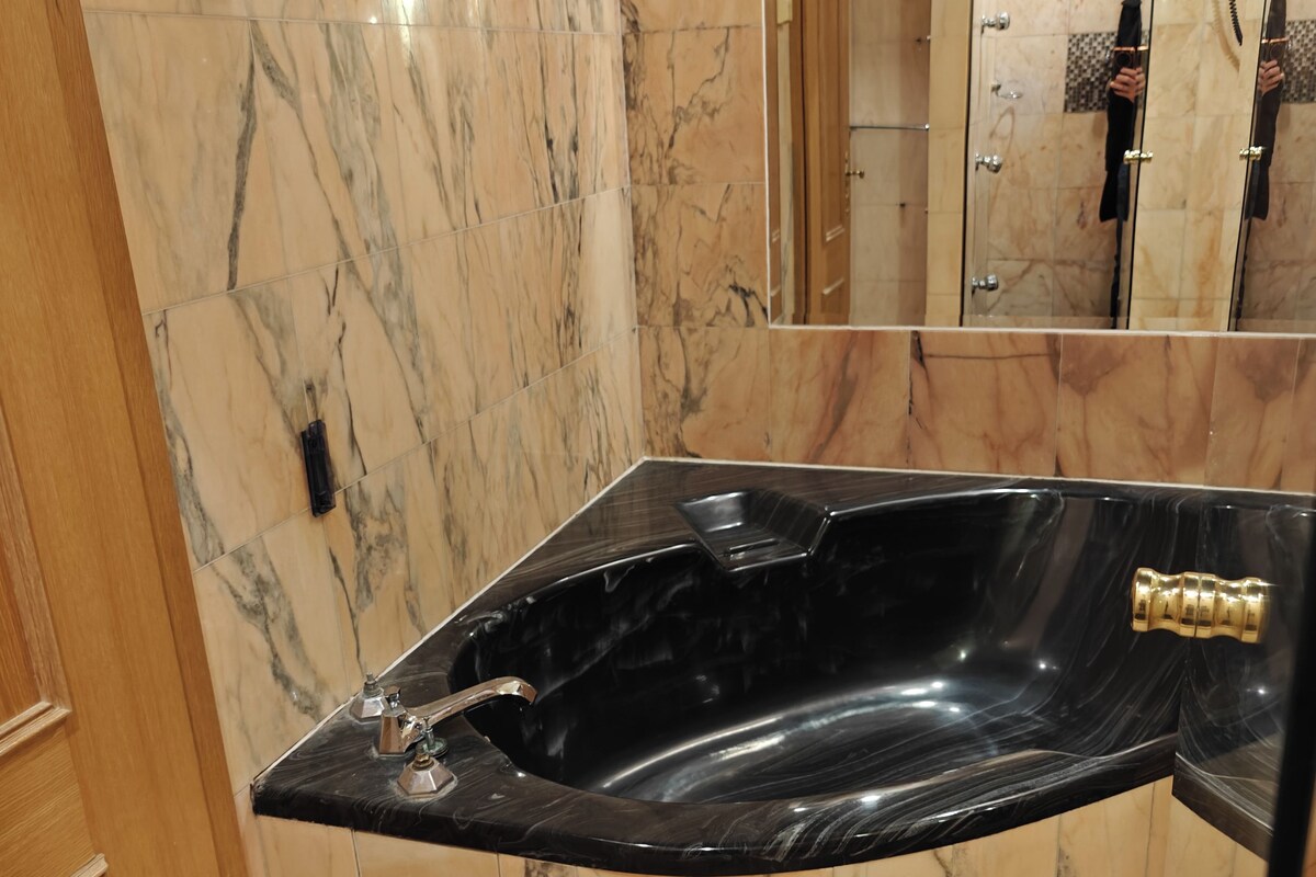 A bathroom with a black marble bathtub, marble walls, and a wooden door.