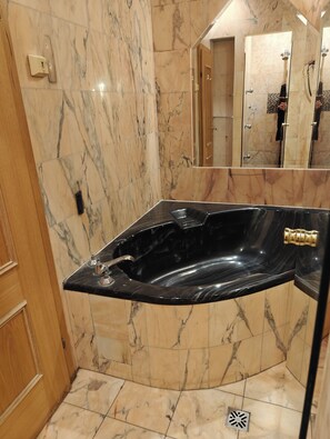 A bathroom with a black marble bathtub, marble walls, and a wooden door. - Hotel Viki (Vienna)