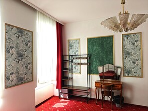 A room with a bunk bed, a desk, a chair, a radiator, and framed tropical leaf artwork.