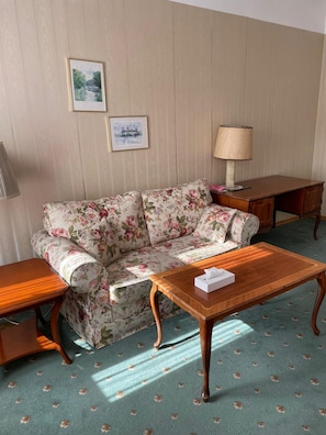 A room with a floral sofa, a wooden coffee table, a lamp, and a framed picture on the wall. - Hotel Viki (Vienna)