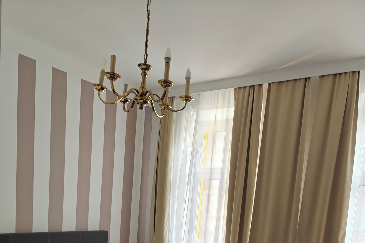 A modern bedroom with a large bed, a chandelier, and a view of the outdoors through sheer curtains.