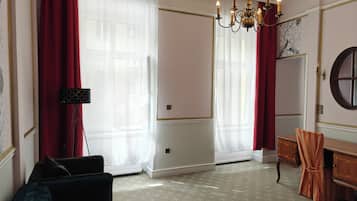 Ein Zimmer mit großem Fenster, einer Kristallleuchtre, einem Spiegel und einer Holzkommode.