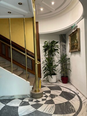 A lobby with a marble floor, a staircase with golden railings, and potted plants. - Hotel Viki (Vienna)