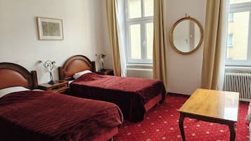 A hotel room with two beds, a wooden table, a round mirror, and a window with curtains.