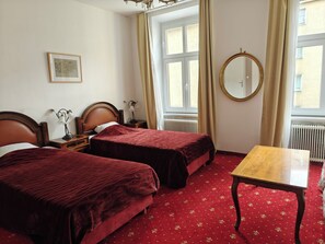 A hotel room with two beds, a wooden table, a round mirror, and a window with curtains.