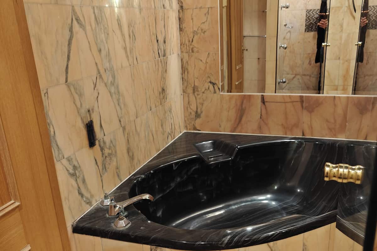 A bathroom with a black marble bathtub, marble walls, and a wooden door.