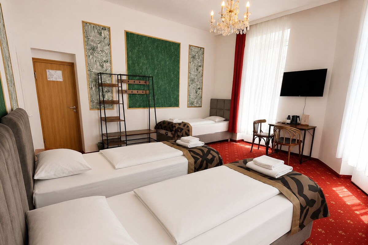 A hotel room with two beds, a desk, a television, and a red carpeted floor.