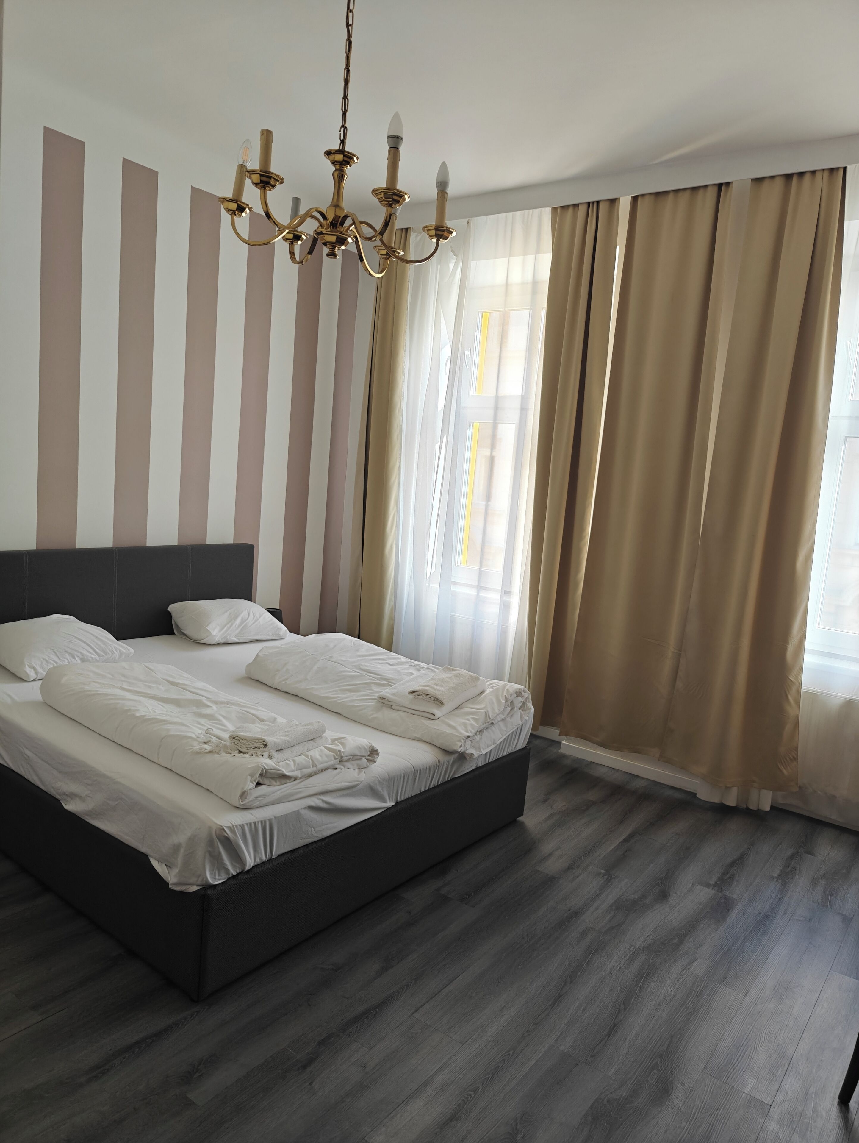 Ett modernt hotellrum med en stor säng, en kristallkrona och randiga väggar.