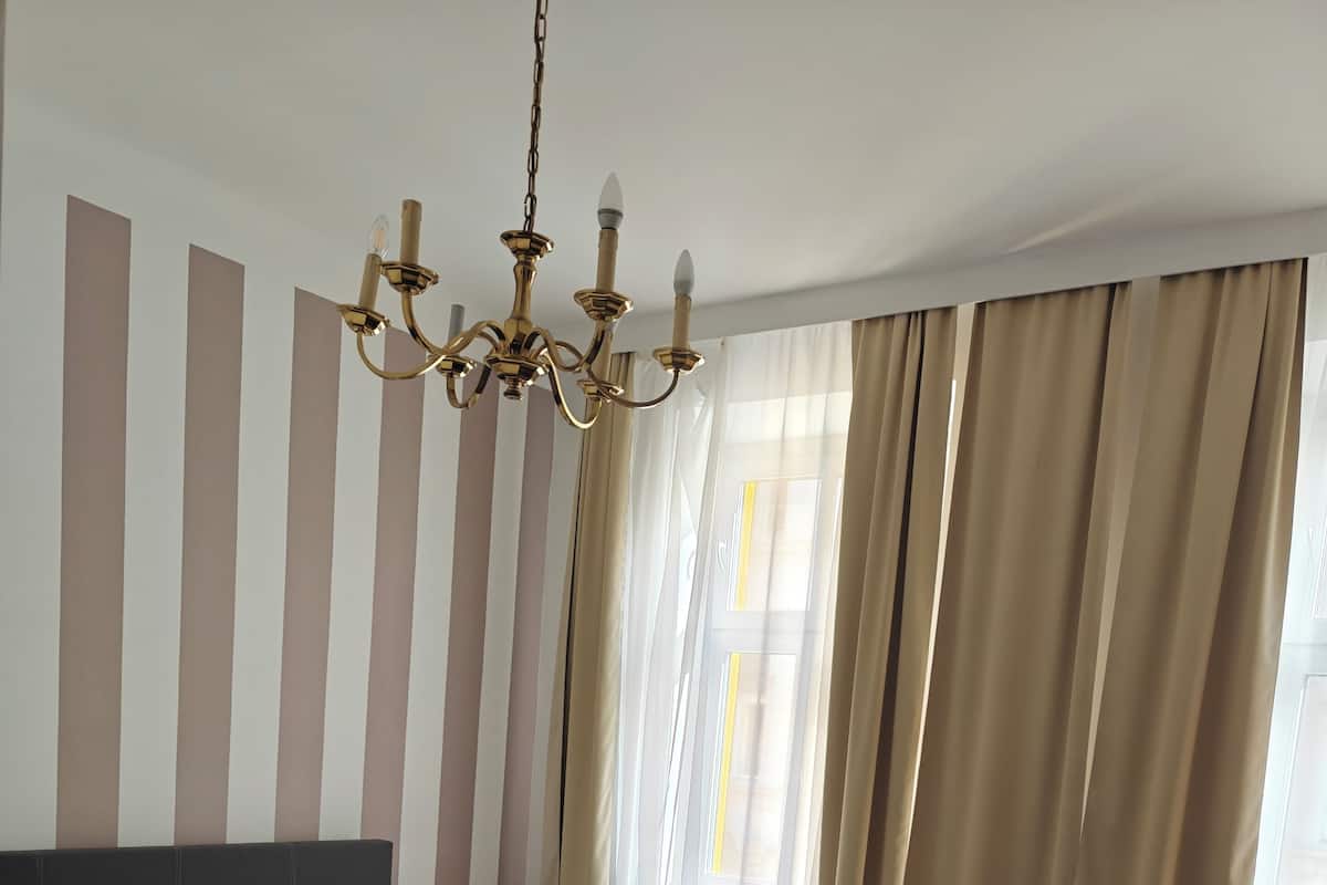 A modern bedroom with a large bed, a chandelier, and a view of the outdoors through sheer curtains.