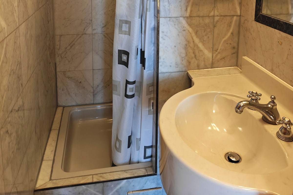 A bathroom with a shower, a sink, and a towel rack.