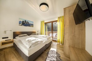 A modern bedroom with a large bed, a TV mounted on the wall, and a window with yellow curtains. - Luxury Alpine Chalet in Neukirchen (Neukirchen am Grossvenediger)