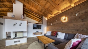 Ein modernes Wohnzimmer mit Holzboden, einem grauen Sofa, einem Holztisch und einem Kamin.