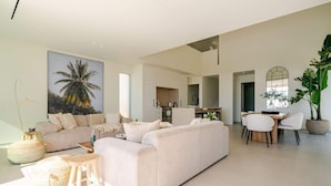 A spacious living area with a large sofa, a dining table with chairs, and a kitchen in the background.