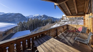 Una terraza de madera con bancos y sillas que da a un paisaje montañoso nevado.