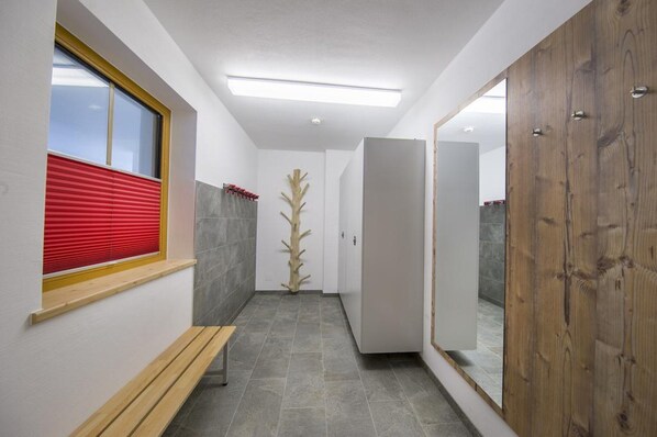 Un couloir avec un banc, une porte en bois, une fenêtre fermée par un store rouge et une grande plante.