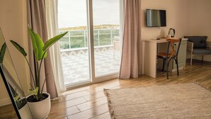A room with a balcony, a potted plant, a desk with a chair, a television, and a sofa. - Koi Ayvalık (Ayvalik)