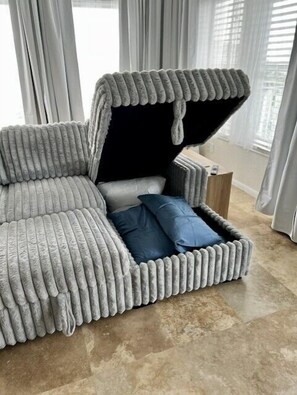 A gray, textured sofa with a built-in storage compartment and a small table beside it.