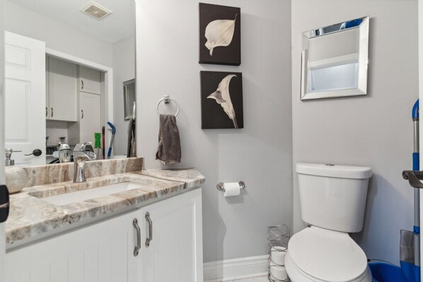 Une salle de bain avec des toilettes blanches, un lavabo doté d’un plan-vasque en marbre et deux miroirs fixés au mur.