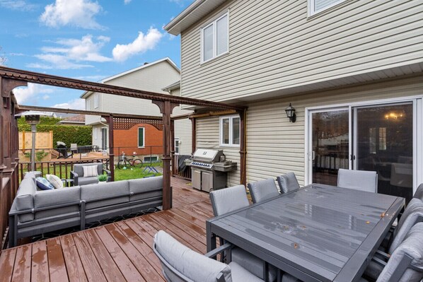 Eine überdachte Terrasse mit Holzboden, Sitzgelegenheiten im Freien und einem Grillbereich.