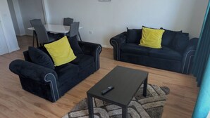 Ein Wohnzimmer mit zwei dunklen Sofas, einem Couchtisch und einem Esstisch mit Stühlen.