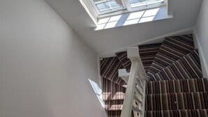 Ein Zimmer mit geneigter Decke, einem Oberlicht, einer weißen Treppe und Streifenstoren.