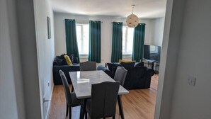 Ein modernes Wohnzimmer mit Esstisch, Sofas und einem Fernseher.