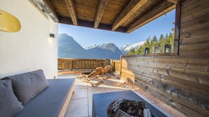 A wooden deck with a sofa and lounge chairs, a fire pit, and a mountain view. - Chalet Retreat With Terrace & Sauna (Neukirchen am Grossvenediger)