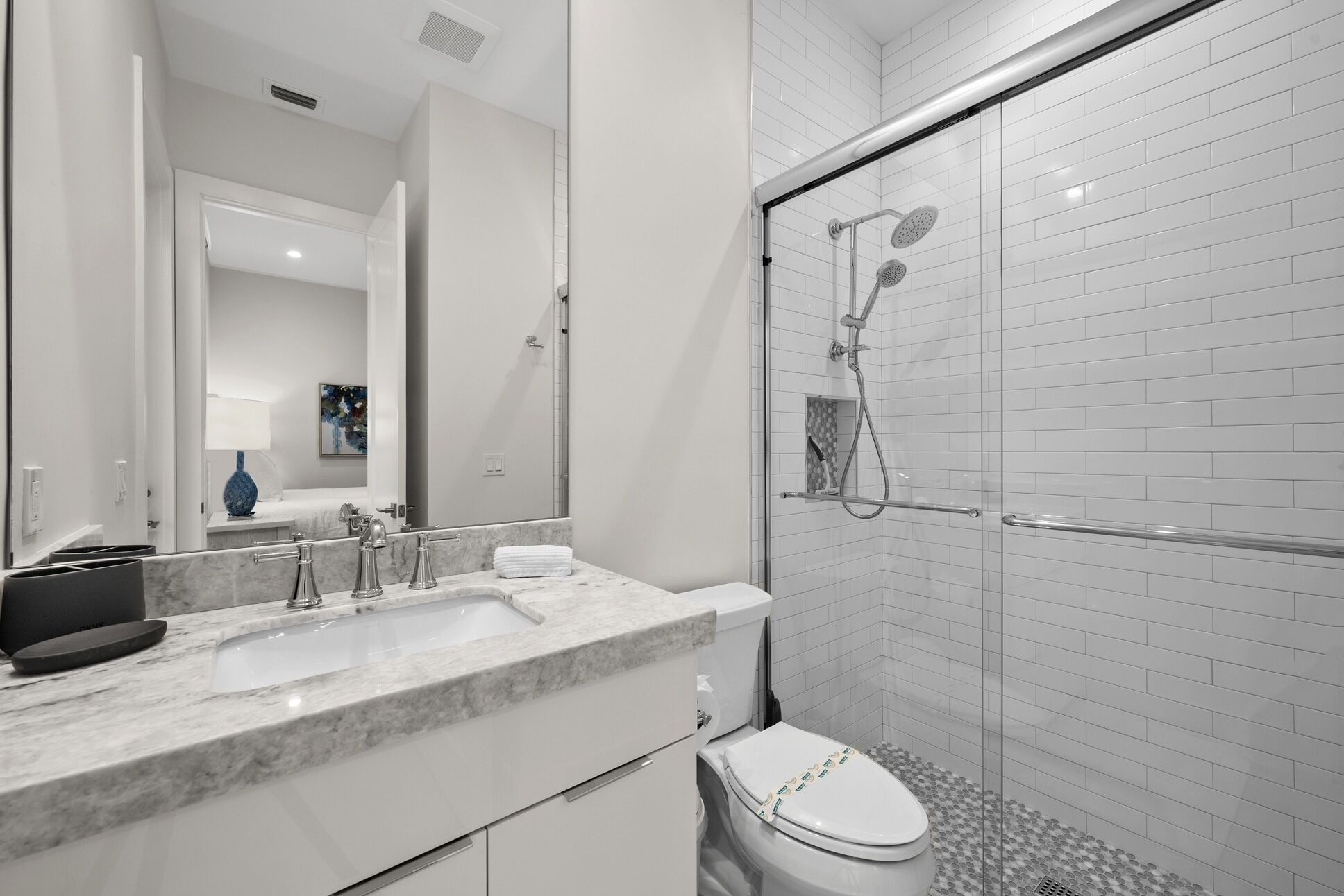 A modern bathroom with a marble sink, a glass shower enclosure, and a toilet with a decorative lid.