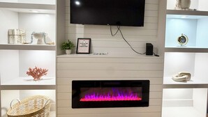 A living room with a mounted TV, fireplace, and shelves with decorative items. - Charming 3-bedroom House - Two Blocks from the Beach (Ventnor City)