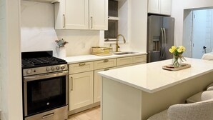 A modern kitchen with white cabinets, a stainless steel refrigerator, a built-in oven, and a central island. - Charming 3-bedroom House - Two Blocks from the Beach (Ventnor City)