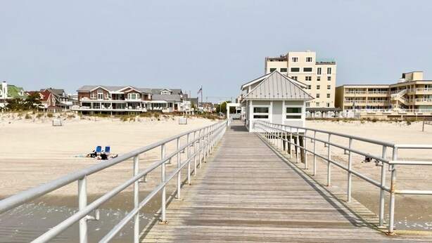 A wooden boardwalk leading to a beach with a lifeguard station and buildings in the background. - Charming 3-bedroom House - Two Blocks from the Beach (Ventnor City)