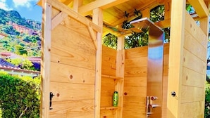 A wooden outdoor shower structure with a door, a showerhead, and a shelf with a bottle. - Costa Rei - House 500 meters from the sea, climate, sea view terrace and garden  (Costa Rei)