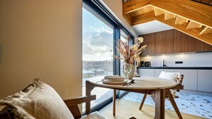 Een moderne keuken met houten kastjes, een eethoek met een ronde tafel en stoelen, en een groot raam met uitzicht op de omgeving.