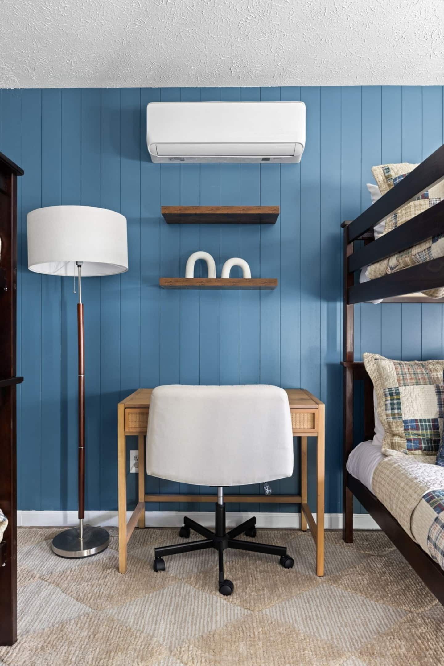 A room with a desk, chair, bunk bed, and an air conditioning unit.