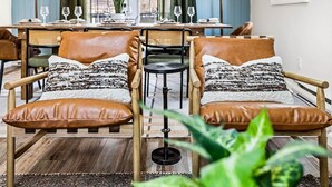 A dining area with two leather armchairs, a small round table, and a dining table set for four. - Escape to the Poconos | Hot Tub, Sauna, Mini-Golf (East Stroudsburg)