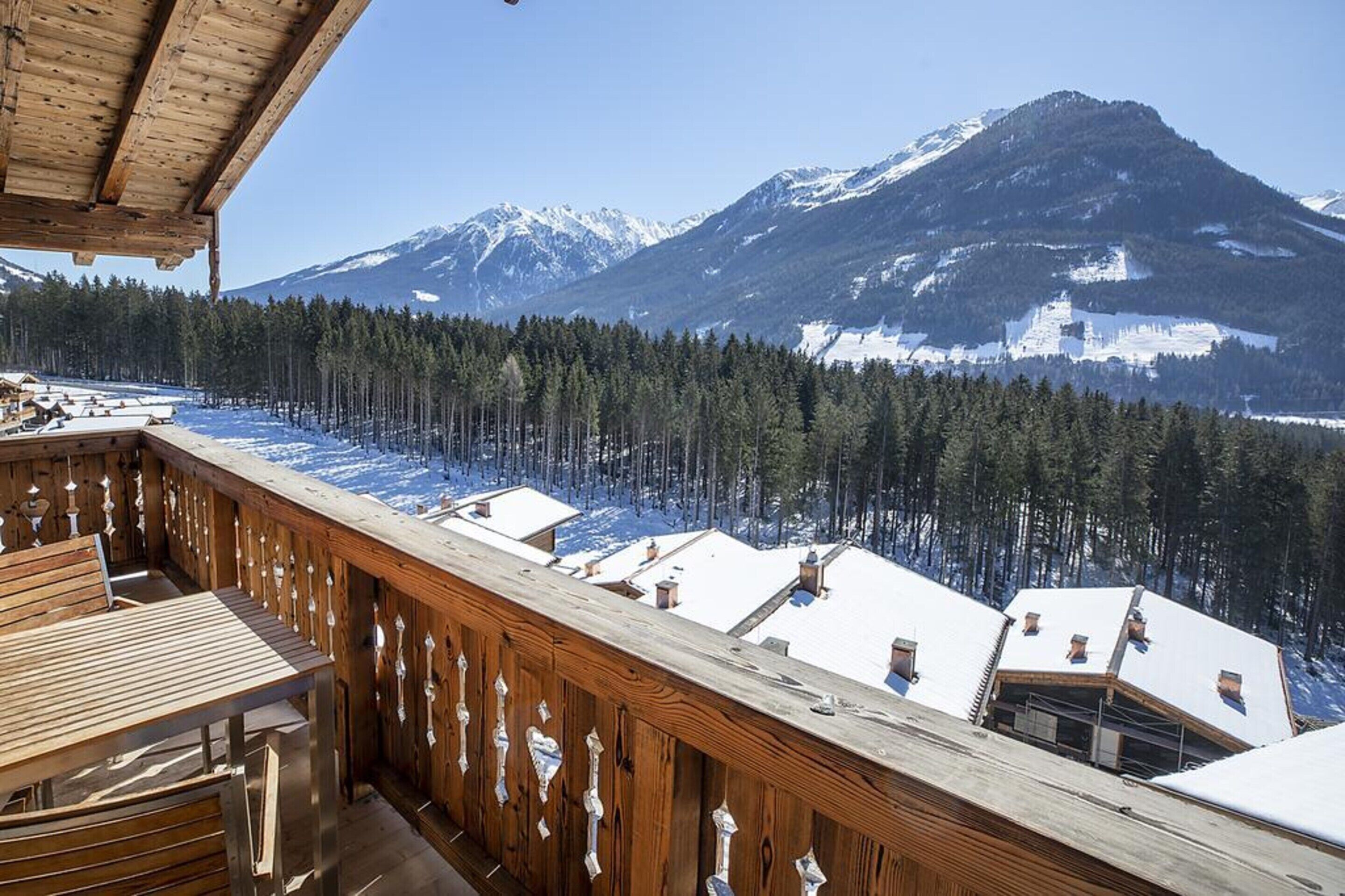 Eine Holzterrasse mit Blick auf schneebedeckte Berge und einen Wald.