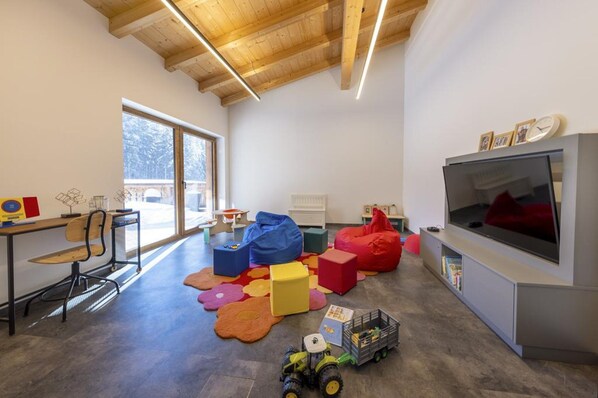 A modern living room with a large TV, wooden ceiling beams, and a view of the outdoors. - Chalet in Neukirchen Near Ski Lift & Sauna (Neukirchen am Grossvenediger)
